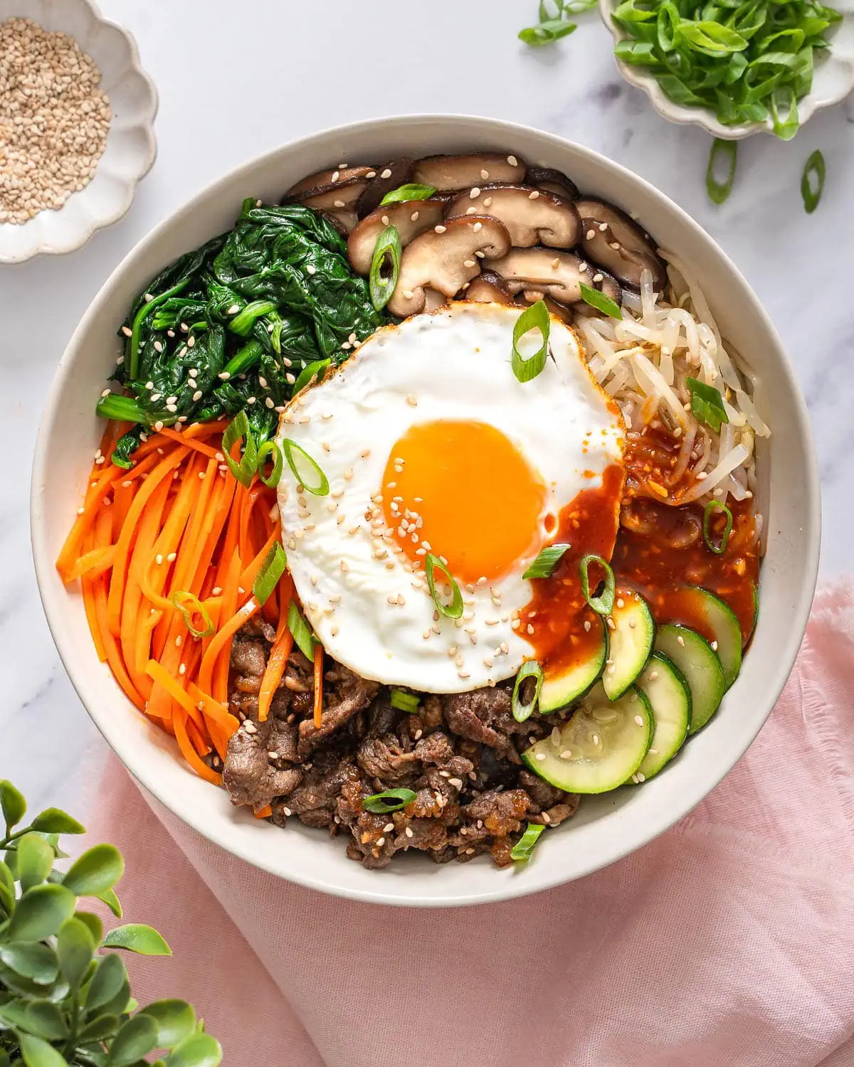 A homemade bibimbap bowl topped with a fried egg, sautéed vegetables and a spoonful of gochujang sauce