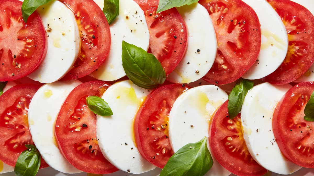 A plate of classic insalata caprese with buffalo mozzarella, ripe tomatoes, and fresh basil on a white dish